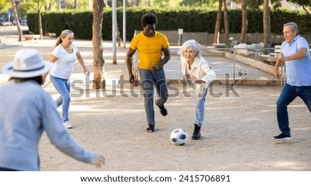 Cheerful males and females kicking the ball in summer park