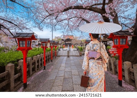 Young Japanese woman in a  traditional Kimono dress strolls by Rokusonno shrine during full bloom sakura cherry blossom period in Kyoto, Japan Royalty-Free Stock Photo #2415721621