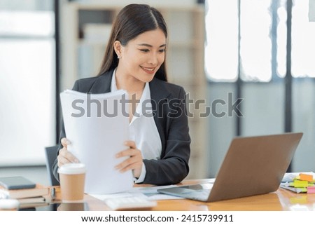Shot of a young professional woman sitting at desk in front of laptop and using mobile phone working on business contract.