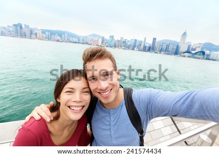 Selfie - Tourists couple taking selfportrait picture photo in Hong Kong enjoying sightseeing on Tsim Sha Tsui Promenade and Avenue of Stars in Victoria Harbour, Kowloon, Hong Kong. Travel concept.