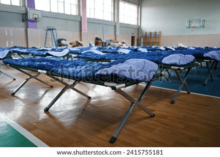 Cots with sleeping bags are placed in the school gym during an emergency Royalty-Free Stock Photo #2415755181