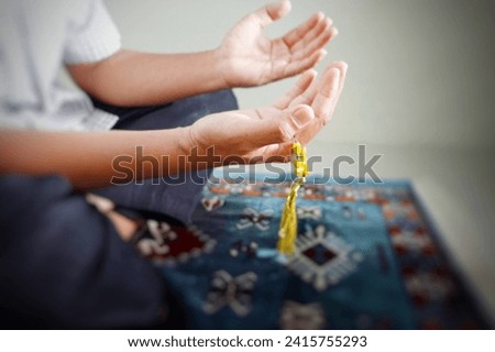 A Muslim man sits on a prayer mat and prays with open hands facing upwards.