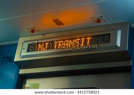An orange digital train display reads "NJ Transit" on one of the system's trains surrounded by a blue hue Royalty-Free Stock Photo #2415758021