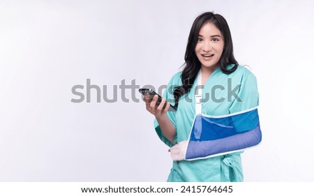 Injured asian woman painful accident broken hand soft splint arm looking screen mobile phone standing on white background. Smile young girl hold smartphone over isolated.Insurance accident health care