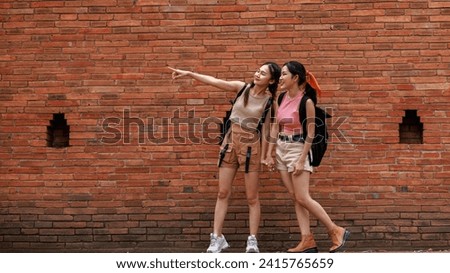 two asian tourist girl standing posing and pointing hand at the tha phae gate, chiang mai thailand, travel destination concept,