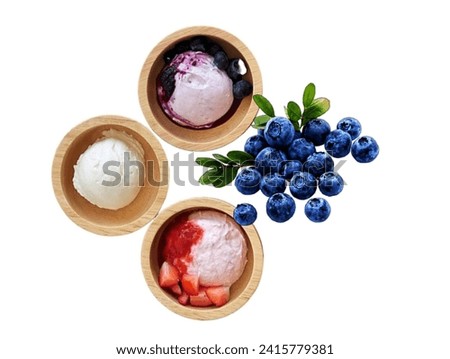 In the picture is ice cream in a brown wooden cup. There are milk, strawberry, and blueberry ice creams. There are five cups in three flavors, and there are strawberries and blueberri