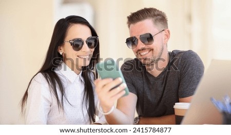 Portrait of couple watch memorable pictures on smartphone, go through pics from holiday. Man and woman smile, warm memories. Happiness, memory concept