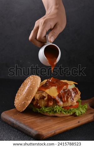 A man's hand pouring sauce on the appetizing burger Royalty-Free Stock Photo #2415788523