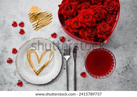 The banner. Table setting. Stylish ceramic plate, glass of red wine, red roses, fork and golden hearts on a concrete background. The concept of celebrating Valentine's Day for cafes and restaurants. Royalty-Free Stock Photo #2415789737