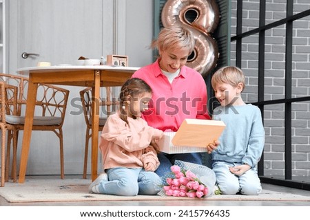 Little children and their grandmother opening gift box in kitchen. International Women's Day Royalty-Free Stock Photo #2415796435