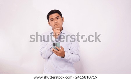 Asian man scratch his head while holding mobile phone and showing confused face expression against white background