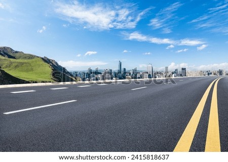 Asphalt road and green mountain with city skyline landscape under blue sky. high angle view.