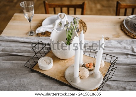 Easter decor with candles, easter quail eggs in nest, vase with flowers at home. Setting table for Easter festive dinner. Holidays celebration concept. Interior design of easter dining room. Closeup.