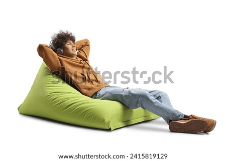 Guy with headphone resting on a green bean bag armchair isolated on white background Royalty-Free Stock Photo #2415819129