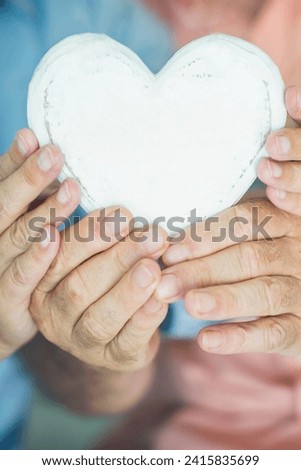 Close up of heart shape wooden decoration object. Concept of healhty senior lifestyle. Heart attack concept. Love and relationship with old mature man and woman hands. Together forever life. Dating