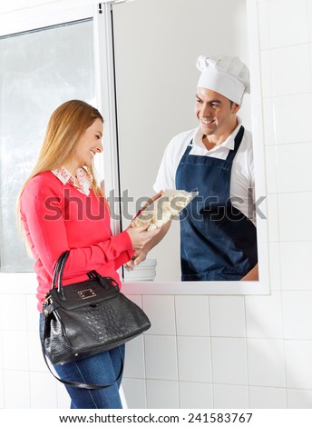 Happy woman purchasing uncooked ravioli pasta packet from chef through window