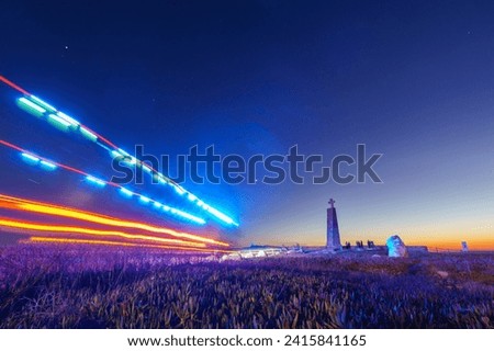 Long exposure of fire truck with blue lights driving to cross on a stone pillar at Cabo da Roca under the night sky, Sintra, Lisbon, Portugal