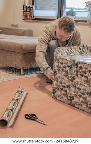 a man at home packs a large box with a gift in decorative paper