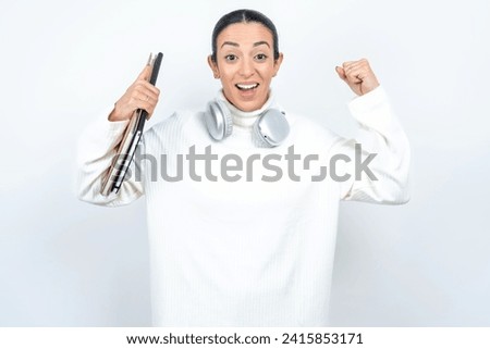 Shocked ecstatic Young beautiful woman wearing white sweater win luck lottery raise hands up shout yea