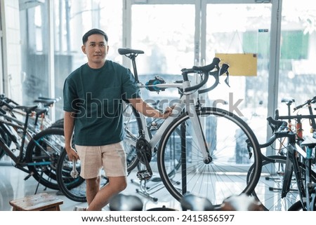 Asian male employee stands holding a wrench next to a new bike while working at a bike shop