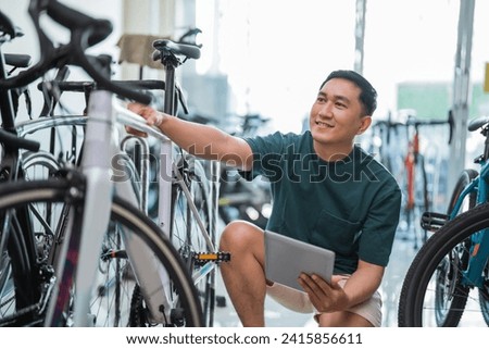 young male employee using a tablet while checking a bicycle frame at a bicycle shop