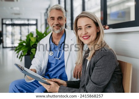 Pharmaceutical sales representative presenting new medication to doctor in medical building, looking at camera. Royalty-Free Stock Photo #2415868257