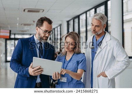 Pharmaceutical sales representative talking with doctors in medical building, presenting new product on tablet. Royalty-Free Stock Photo #2415868271