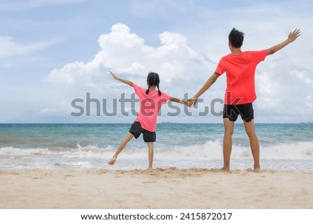 Picture of brother and sister stand hold hands Spread your arms out on each side. and facing the sea with waves crashing against it They had fun and enjoyed their special holiday trip with families.