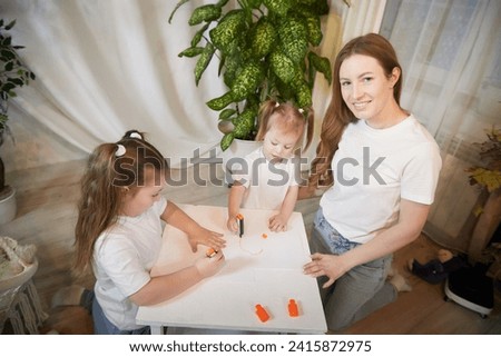 Young mother or babysitter, little daughter, sister teenager girl drawing at table in room. Painting, doing homework, family enjoying leisure at home