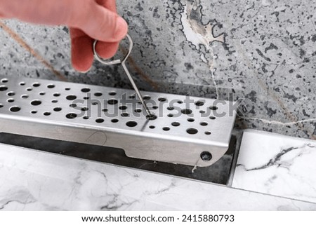 Hand open linear shower drain system using hook. Royalty-Free Stock Photo #2415880793