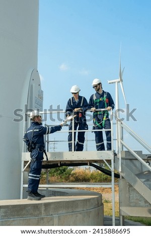 Vertical image professional technican worker give the document to his coworkers stand in base of windmill or wind turbine also discuss about work.