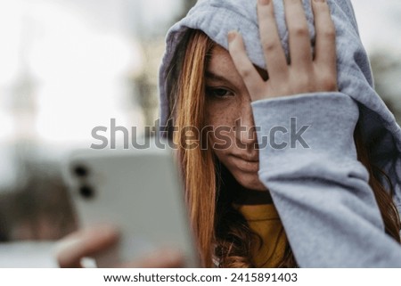 Portrait of teenage girl looking at her smartphone, sad, anxious, alone. Cyberbullying, girl is harassed, threated online. Royalty-Free Stock Photo #2415891403