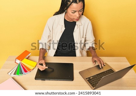 Indonesian designer with graphic tablet, PC, and color palette on yellow studio