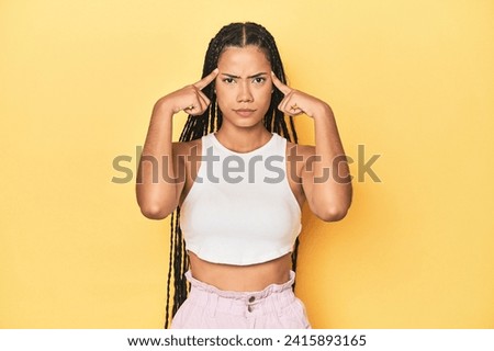 Young Indonesian woman on yellow studio backdrop focused on a task, keeping forefingers pointing head.