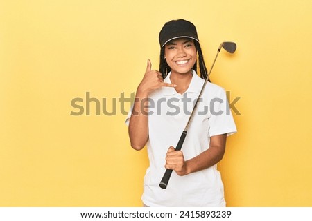 Indonesian female golfer on yellow backdrop showing a mobile phone call gesture with fingers.