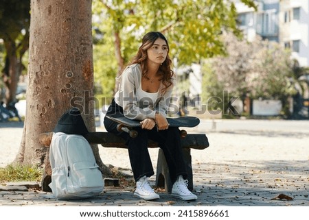 Schoolgirl with skateboard waiting for friends in park to hang out after school