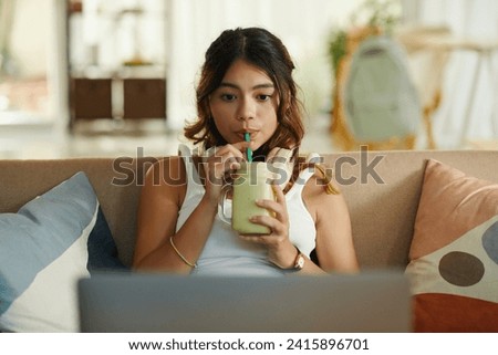 Zoomer girl sipping smoothie and and watching show on laptop Royalty-Free Stock Photo #2415896701