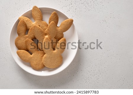Easter cookies shaped of bunny in white plate on white background. View from above. Copy space. Festive food and kids snacks. Greeting card.