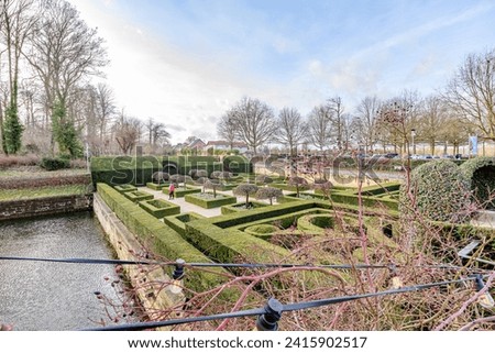 French courtyard of 16th century Alden Biesen castle, seen from bridge from top perspective, tourist with his dog walking among bushes, bare trees in background, cloudy day in Bilzen, Limburg, Belgium