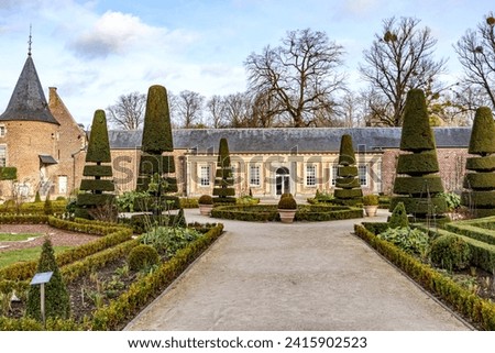 Straight path in French garden with central fountain in Alden Biesen Castle, 16th century building with brick walls and gable roof in background, trees cut into conical shape, Bilzen, Limburg, Belgium Royalty-Free Stock Photo #2415902523