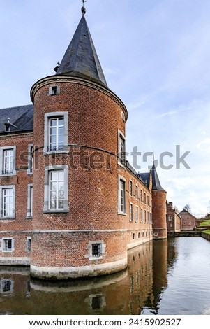 Moat surrounding 16th century Alden Biesen castle, circular tower, brick walls, windows and gable roof, view from outer courtyard, cloudy day in Bilzen, Limburg, Belgium Royalty-Free Stock Photo #2415902527