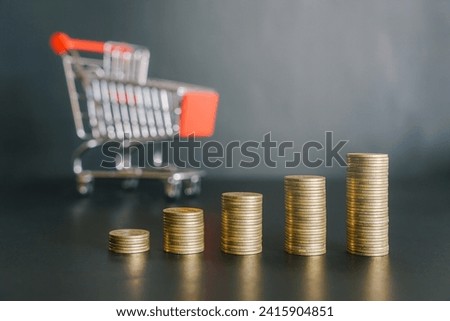 Upward of golden money coin stack on black background with small shopping cart in the background. Business and finance concept. 