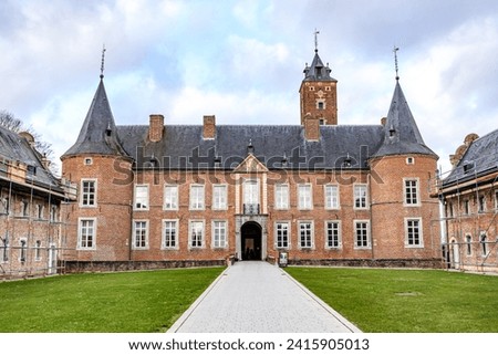 Rear facade of Alden Biesen Castle, brick walls, gable roof tand wo towers, 16th century, straight path in courtyard, cloudy day with stormy sky in Bilzen, Limburg, Belgium Royalty-Free Stock Photo #2415905013