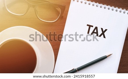 TAX - text on paper with cup of coffee and glasses on wooden background in sinlight.