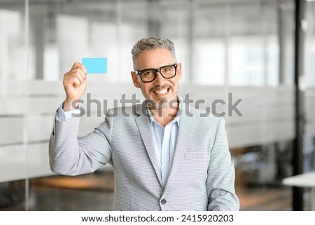 Photo of cheerful grey-haired elegant businessman demonstrate debit card and smiling toothy, successful 50s manager ceo investor got a profit, e-commerce concept
