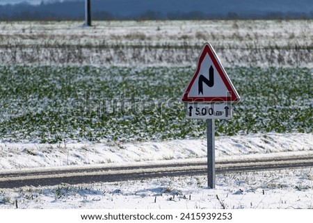Snowy countryside landscape with sunshine and a road sign, dangerously slippery
