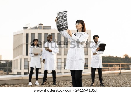 Multiethnic employees of medical clinic working on distant devices with results of examination of patients. Portrait of Caucasian doctor holding x-ray scan of patient during break outdoors hospital.