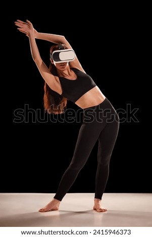 Portrait of young woman in sportwear doing exercises for back in virtual reality glasses against back studio background. Concept of sport, dieting, body care and active lifestyle.