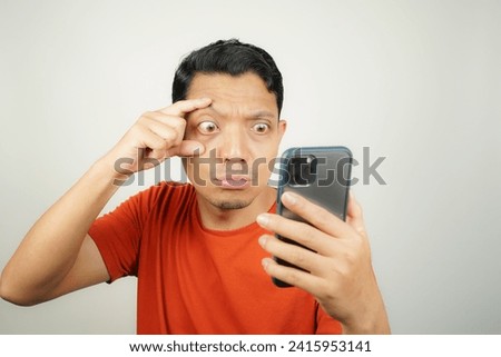 Wow face of Asian man in orange t-shirt shocked what he see in the smartphone on isolated background