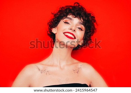 Young beautiful smiling female in trendy summer black tank top. Carefree woman posing near red wall in studio with curly hairstyle. Positive model having fun. Cheerful and happy